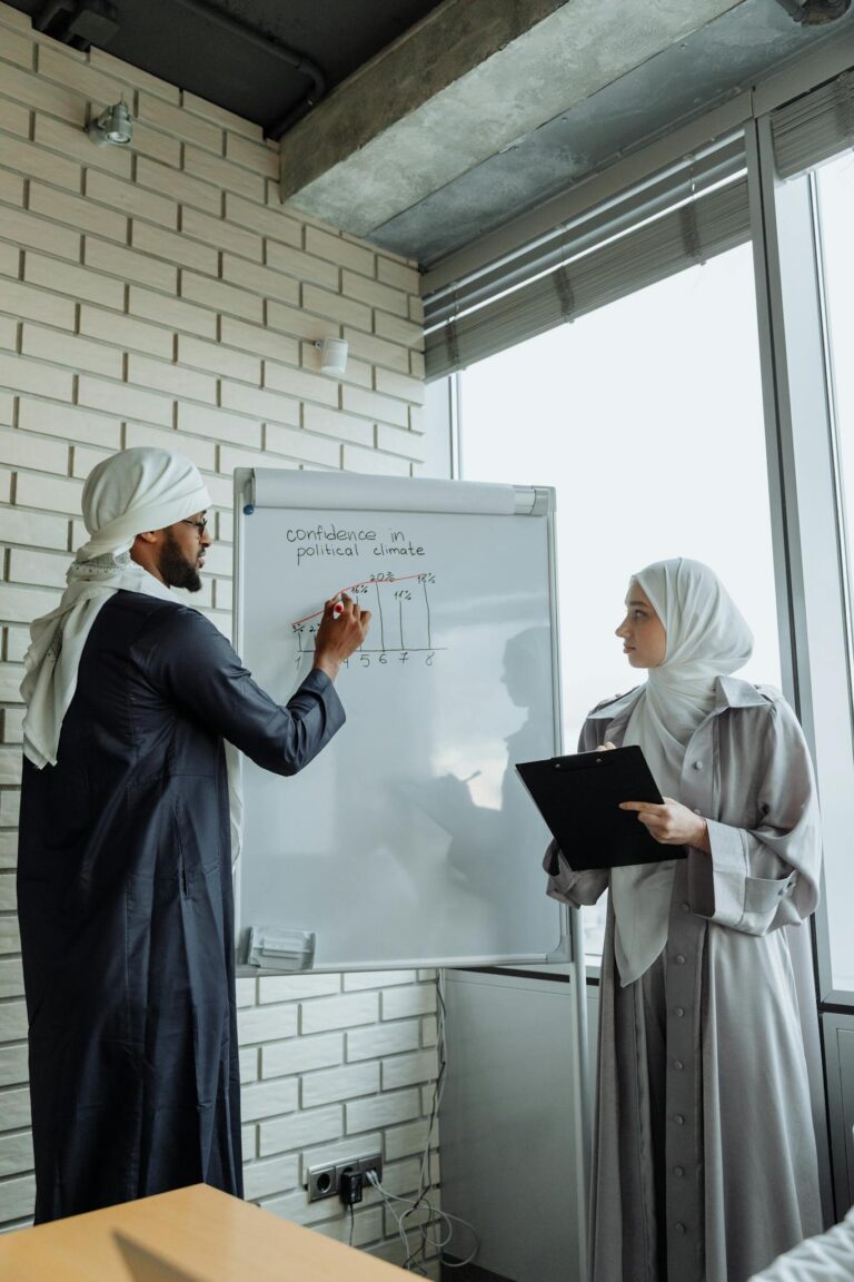 Two professionals in traditional attire collaborate during a business presentation in an office.